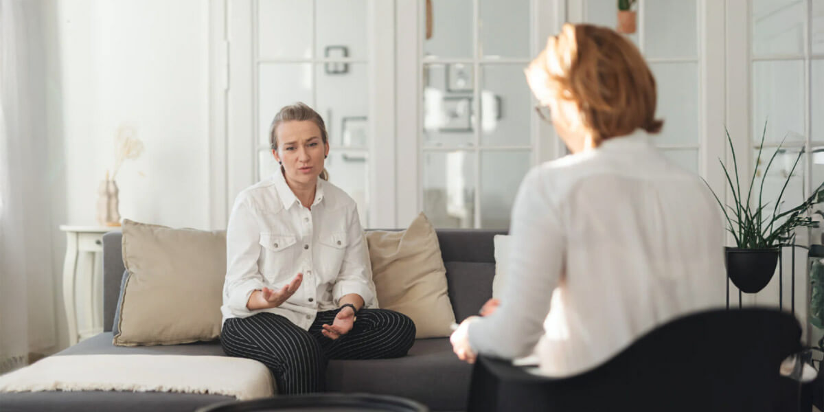 A woman speaks with a therapist in a one-on-one session, expressing concerns in a calm, supportive clinical setting.