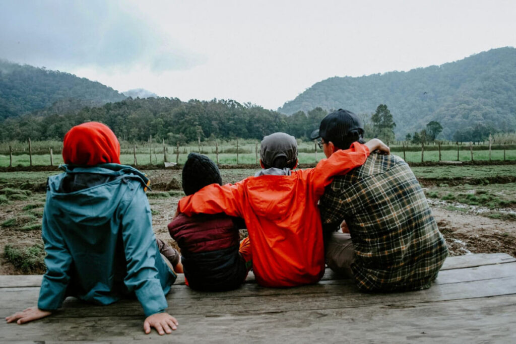 A group of people sitting together outdoors with arms around one another, representing connection, family support, and community during the recovery journey.