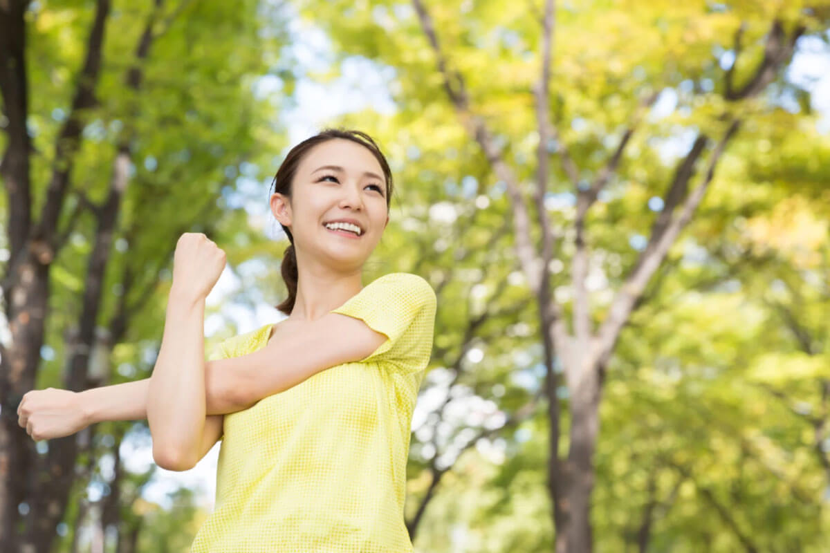 A woman stretching outdoors in a sunlit park, representing healthy lifestyle habits, wellness, and positive daily routines that support long-term recovery.