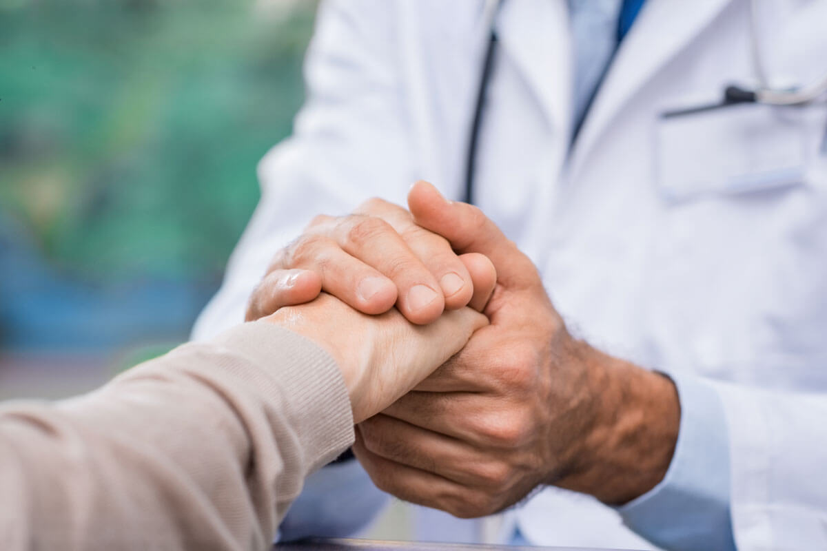 Close-up of a doctor in a white coat holding and reassuring a patient's hand.