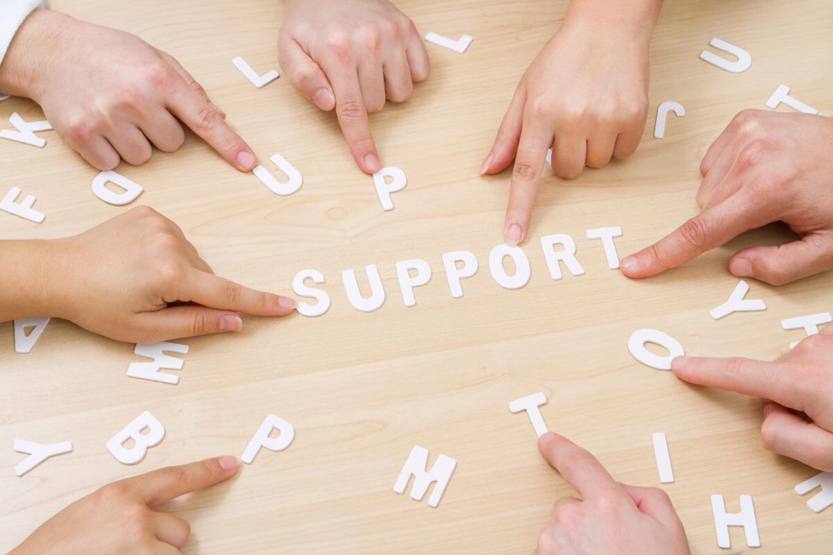 Overhead view of several hands pointing to letters spelling out the word support.