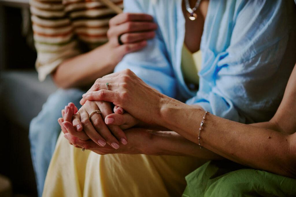 Close up of clasped hands resting together in a comforting gesture between two people.