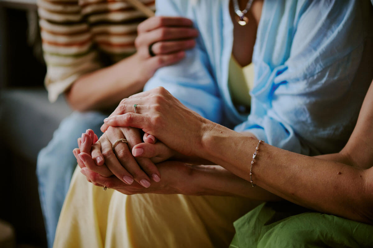 Close up of clasped hands resting together in a comforting gesture between two people.